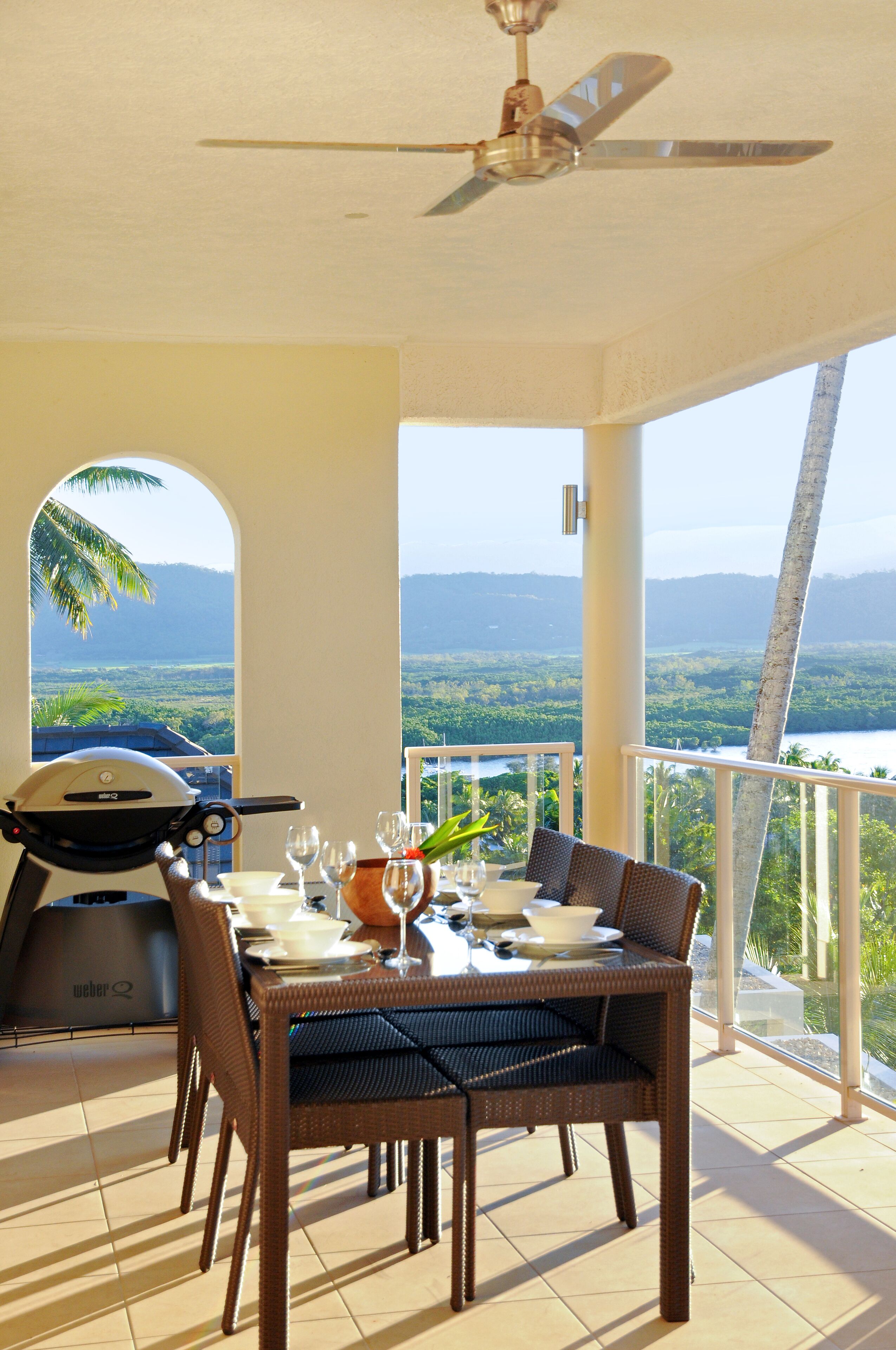 Un espace extérieur aménagé pour les repas, avec une table pour quatre personnes, un ventilateur de plafond et un barbecue.