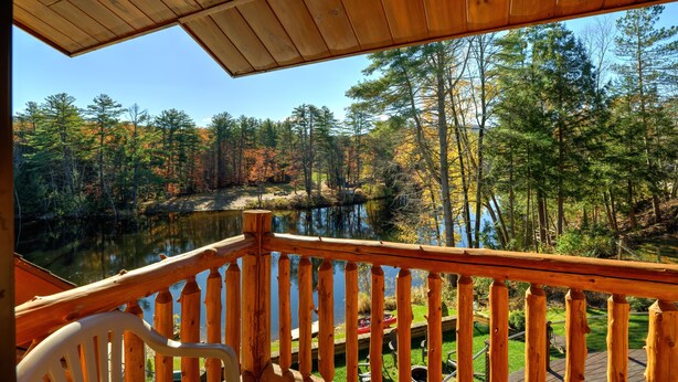 Une terrasse en bois, dotée d’une balustrade, qui offre une vue sur un lac entouré d’arbres aux couleurs automnales.