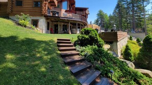 Une cabane en rondins avec des fondations en pierre, une terrasse en bois et un escalier menant à un porche abrité.