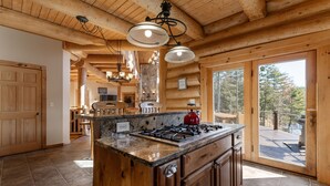 Une cuisine dotée d’un îlot central, de poutres en bois au plafond et d’une porte vitrée donnant sur une terrasse extérieure.
