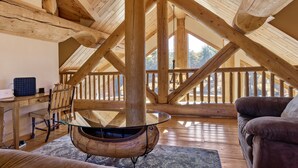 Un intérieur en bois avec une table en verre, des poutres apparentes et une vue depuis un balcon.