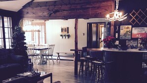 A cozy interior with wooden beams, a dining area with chairs, a bench, and a kitchen counter with a hanging light fixture. - Lakefront Catskills Lodge (Monticello)