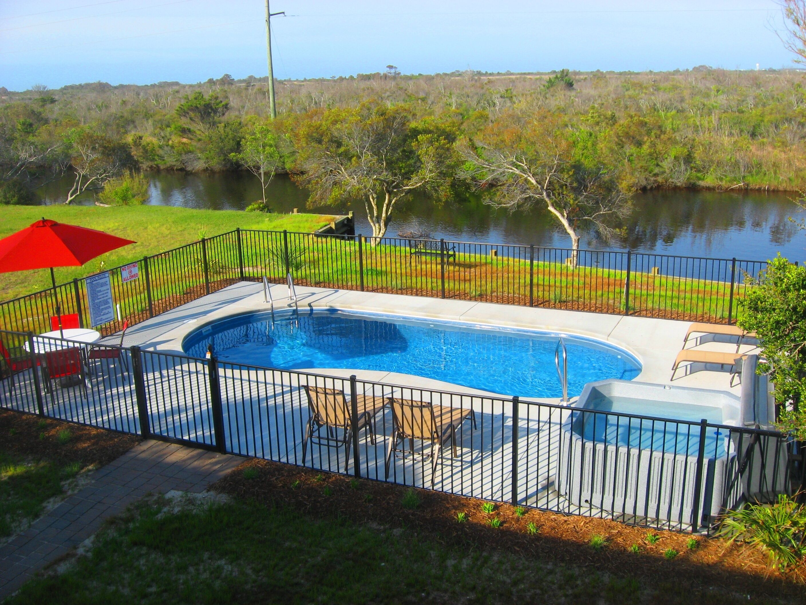 A swimming pool with a surrounding fence, a covered hot tub, and a view of a lake.