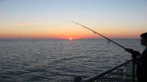 A person fishing at sunset with the sun visible on the horizon.