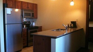 A kitchen with wooden cabinets, a stainless steel refrigerator, a microwave, a stove, and a sink. - 🎿 Ski-In\Out Penthouse. Sunrise 🌅 Mtn ⛰️ Views. Snowshoe’s Most Luxurious Lodge 🌅 (Snowshoe)