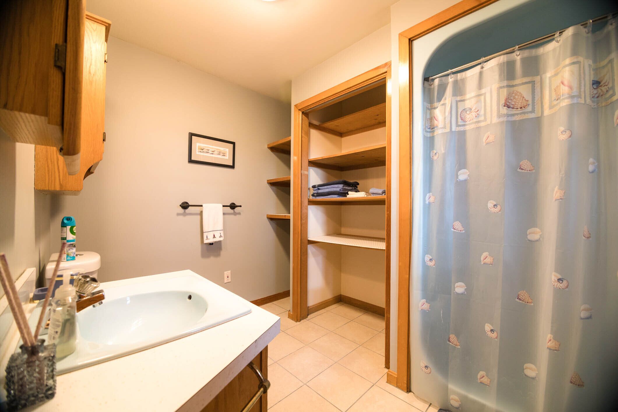A bathroom with a sink, shelves, a toilet, and a shower curtain.