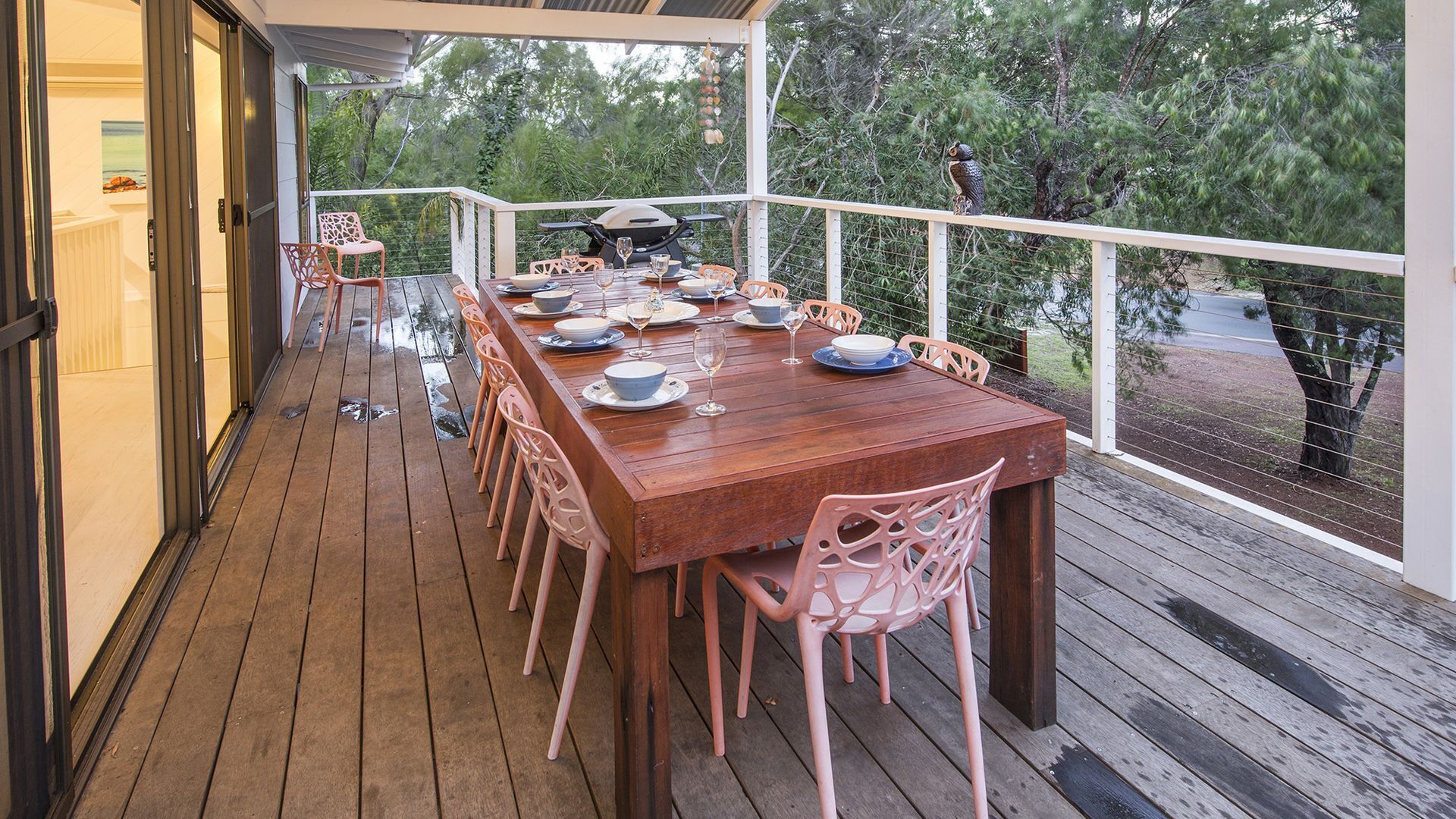 A wooden deck with a dining table set for six, surrounded by pink chairs, overlooking a natural landscape.