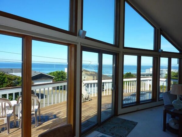Quarto espaçoso com grandes janelas e vista para o oceano, além de área com terraço e mobiliário para área externa.
