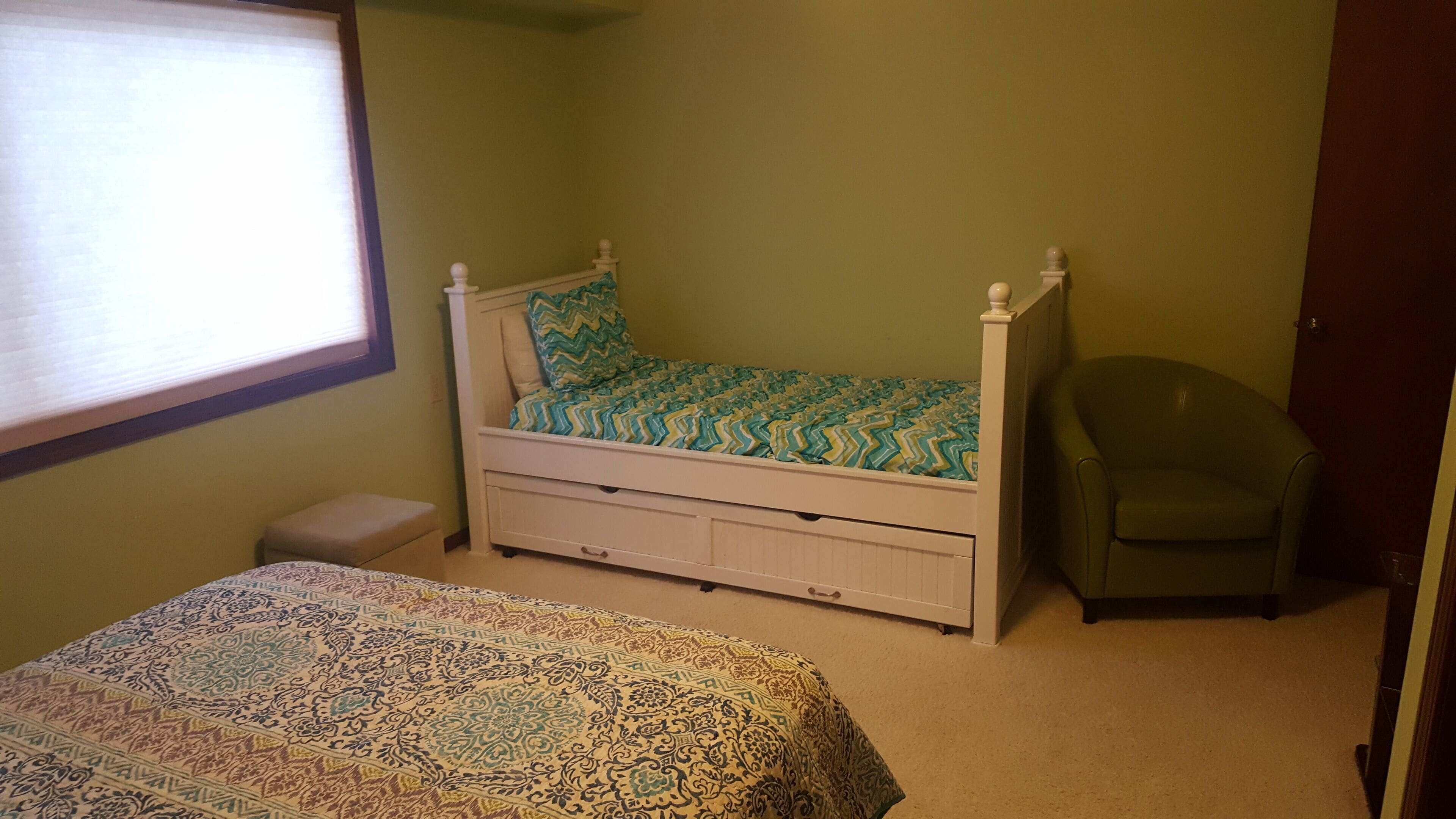 A bedroom with a four-poster bed, a chair, a bedside table, and a window.