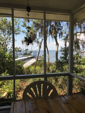 A covered porch with a view of a beach and trees.