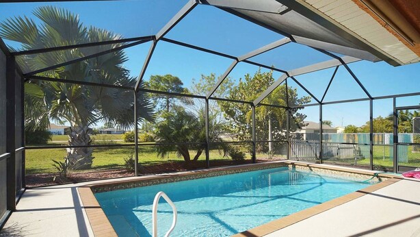 A covered swimming pool with a clear view of the surrounding greenery and a fenced area. - Budget friendly villa; Sleeps 8 w/saltwater pool! Villa Luisa - SWFL Rentals (Cape Coral)