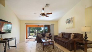 A living room with a TV, a ceiling fan, a sofa, a coffee table, and a patterned rug. - Budget friendly villa; Sleeps 8 w/saltwater pool! Villa Luisa - SWFL Rentals (Cape Coral)