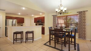 A kitchen with a central island, wooden bar stools, a dining table with chairs, and a chandelier. - Budget friendly villa; Sleeps 8 w/saltwater pool! Villa Luisa - SWFL Rentals (Cape Coral)