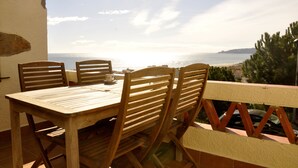 A wooden table and chairs on a balcony overlooking a beach with a clear sky. - Casa Amandina - Seaview House with Shared Pool and Tennis Court (Estartit)