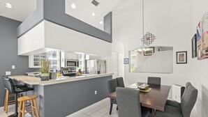 Eine moderne Küche mit weißen Schränken, einer zentralen Kochinsel und einem Essbereich mit einem dunklen Holztisch und grauen Stühlen.