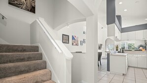 Eine moderne Küche mit weißen Schränken, einer integrierten Kochinsel und einer Treppe mit Teppichstufen zu einer oberen Ebene.
