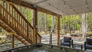 A hot tub with a wooden staircase leading to a covered area with chairs and a forest view. - Modern Creek-front House with Rooftop and Volleyball court (Bushkill)