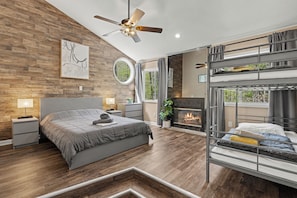 A modern bedroom with a bed, a ceiling fan, a fireplace, and a bunk bed.