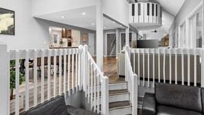 A spacious living area with a staircase, white railings, and a view into the kitchen. - Modern Creek-front House with Rooftop and Volleyball court (Bushkill)