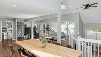 Un vaste espace de vie comprenant une table à manger en bois, des sièges confortables, un téléviseur et un escalier menant à un niveau supérieur.