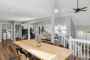 A spacious living area with a wooden dining table, comfortable seating, a television, and a staircase leading to an upper level.
