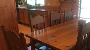A wooden dining table with chairs, a kitchen area with a window, and a small Christmas tree on a shelf.