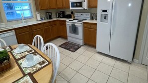 A kitchen with wooden cabinets, a white refrigerator, a microwave, a stove, and a dining table set with plates and cups. - 3 miles Disney, 4 BR/3Ba Pool,Hot tub, game room, Free Wi-Fi,Wheelchair friendly (Kissimmee)