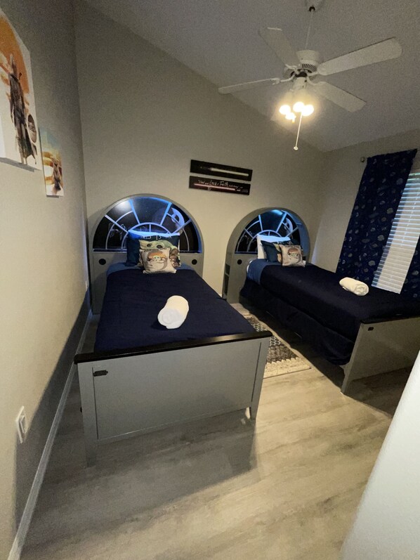 Quarto com duas camas, ventilador de teto e placa na parede.