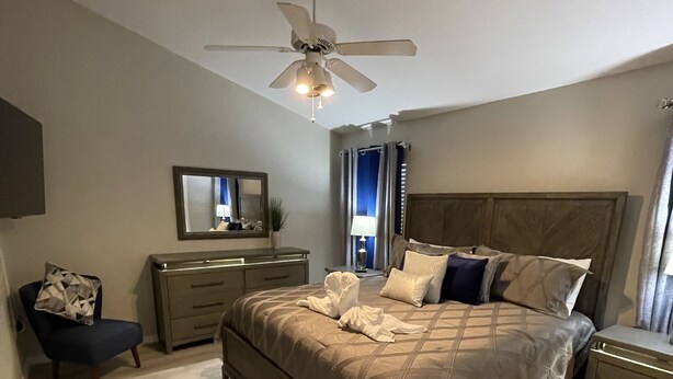 A bedroom with a bed, bedside tables, a dresser, a chair, a ceiling fan, and a window with curtains. - 3 miles Disney, 4 BR/3Ba Pool,Hot tub, game room, Free Wi-Fi,Wheelchair friendly (Kissimmee)