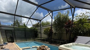 A covered outdoor swimming pool area with a hot tub, lounge chairs, and a stone feature. - 3 miles Disney, 4 BR/3Ba Pool,Hot tub, game room, Free Wi-Fi,Wheelchair friendly (Kissimmee)
