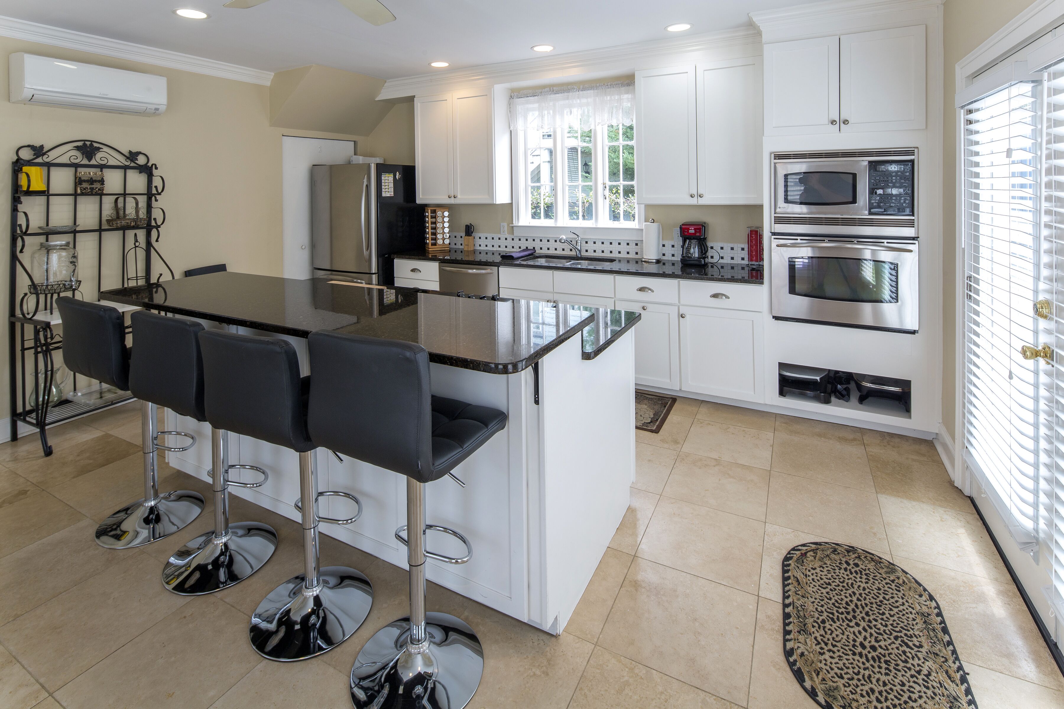 A modern kitchen with white cabinets, stainless steel appliances, a central island with bar stools, and a window providing natural light.