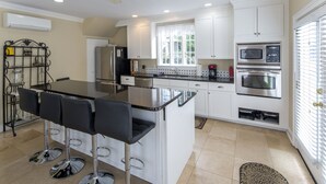 A modern kitchen with white cabinets, stainless steel appliances, a central island with bar stools, and a window providing natural light.