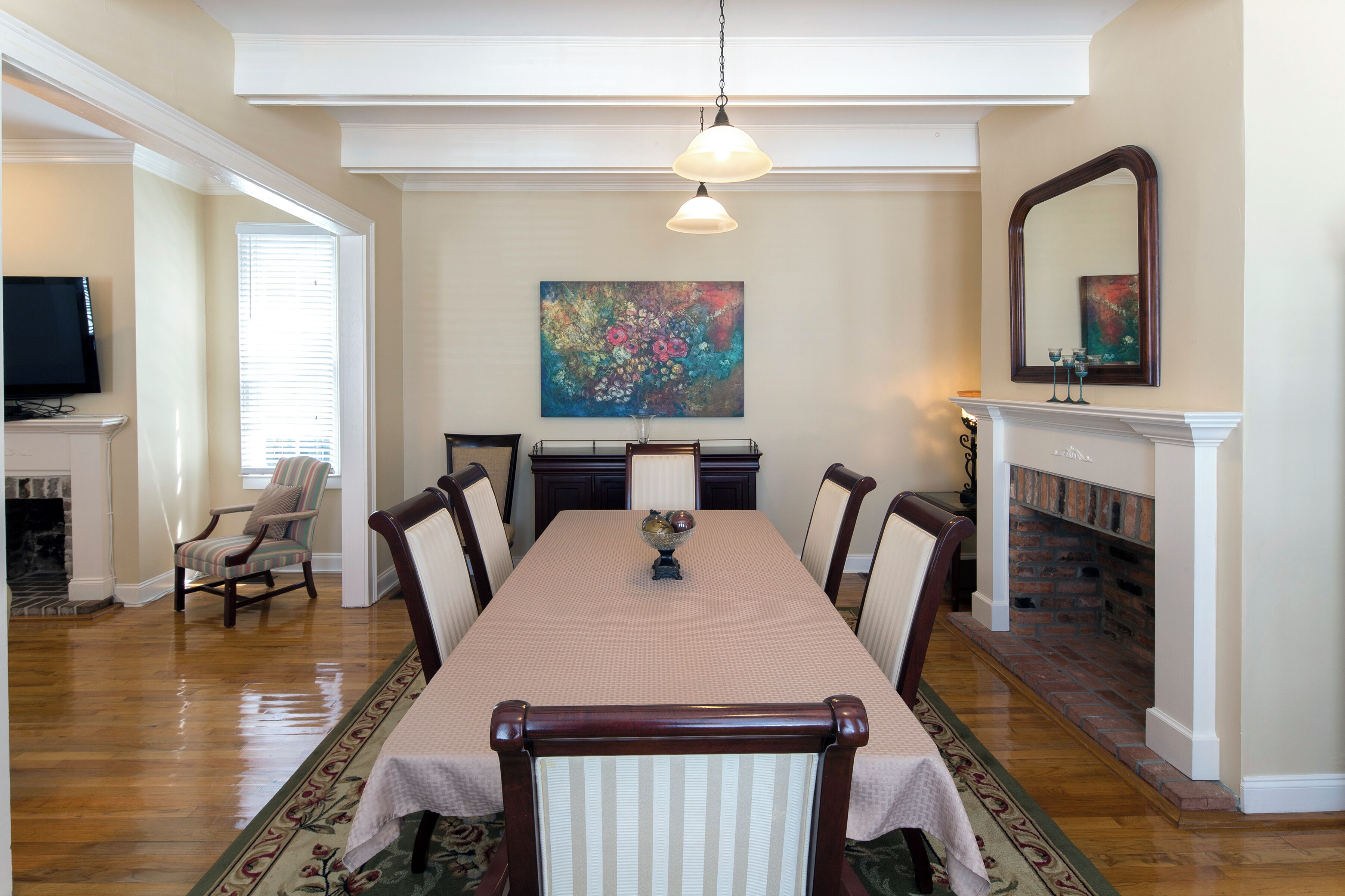 Une salle à manger avec une longue table, des chaises, un téléviseur, une cheminée et un tableau accroché au mur.