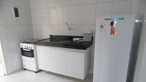 Une cuisine compacte avec des meubles blancs, un plan de travail noir, une cuisinière à gaz, un évier et un réfrigérateur blanc.