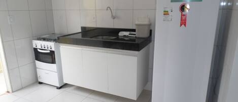 A compact kitchen with white cabinets, a black countertop, a gas stove, a sink, and a white refrigerator.