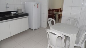 Une cuisine avec des meubles blancs, un réfrigérateur blanc, un plan de travail noir et une table à manger avec des chaises blanches.