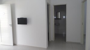 Un couloir avec une porte blanche, un objet noir accroché au mur et un sol carrelé menant à une salle de bain.