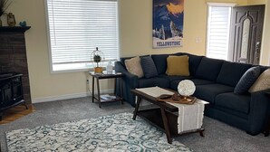 Ein Wohnzimmer mit einem dunkelblauen Sofa, einem gemusterten Teppich, einem kleinen Tisch mit einer Lampe und einem Poster an der Wand.