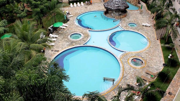 Un área de piscina con varios niveles, piscinas y jacuzzis, rodeada de palmeras y sillas de descanso.
