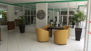Un espacio interior moderno con una pared de vidrio, sillas amarillas, una mesa y plantas en macetas.