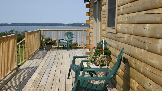 A wooden deck with two green chairs and a table, overlooking a body of water. - Elegant log home with unobstructed ocean views (Cutler)