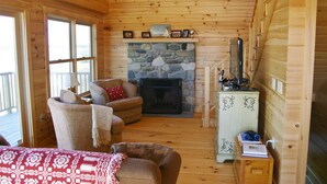 A cozy cabin interior with a stone fireplace, wooden walls, a comfortable seating area, and a small cabinet with items on top. - Elegant log home with unobstructed ocean views (Cutler)