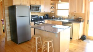 A kitchen with wooden cabinets, a stainless steel refrigerator, a microwave, a stove, and a sink. - Elegant log home with unobstructed ocean views (Cutler)
