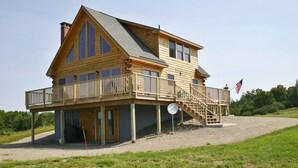 A two-story log cabin with a balcony and a staircase leading to the upper level. - Elegant log home with unobstructed ocean views (Cutler)