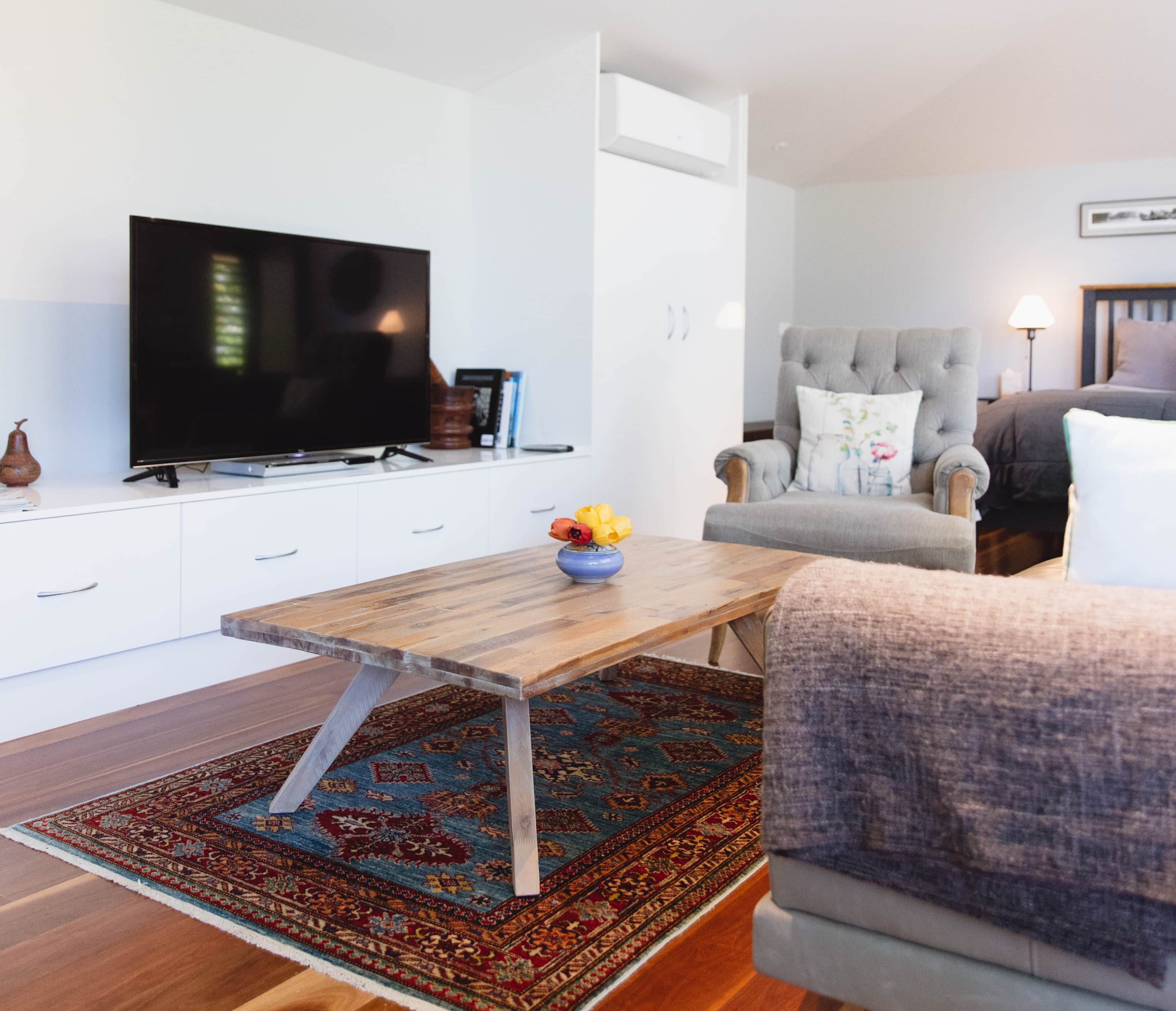 A modern living room with a flat-screen TV, a wooden coffee table, a grey armchair, and a patterned rug.