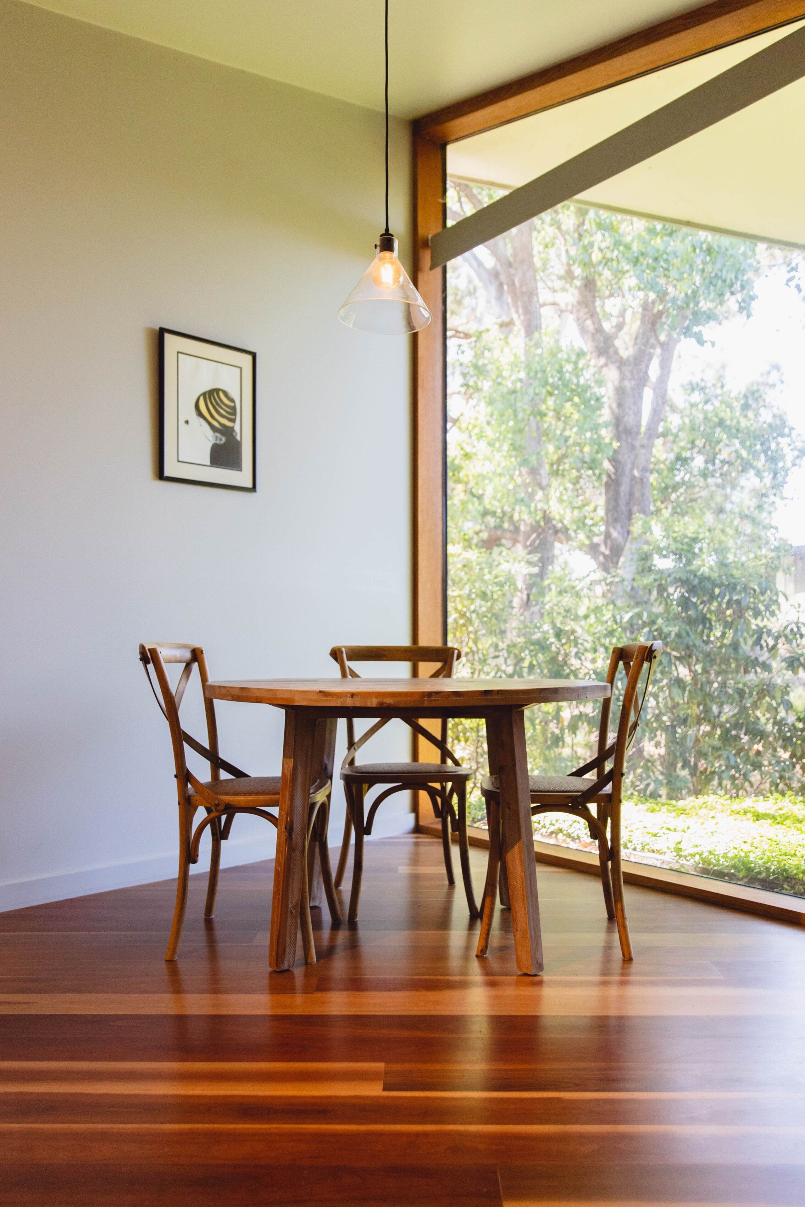 A dining area with a wooden table and chairs, a hanging light fixture, and a framed picture on the wall.