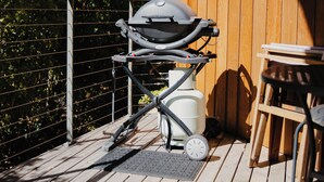 Una terraza de madera con una parrilla, una mesa y sillas.