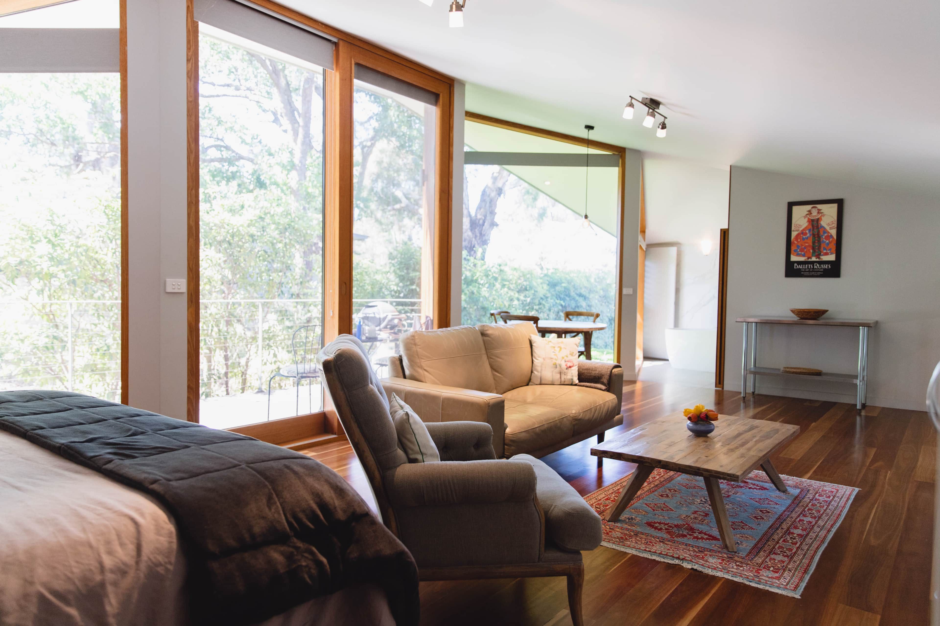 A modern living room with a sofa, armchair, and coffee table. There is a large window providing a view of trees.