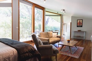A modern living room with a sofa, armchair, and coffee table. There is a large window providing a view of trees. - Glan-y-mor Studio in Metung, Glan-y-mor Studio in Metung (Metung)