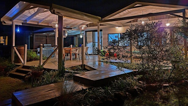 A covered outdoor area with a wooden deck, seating, and potted plants.